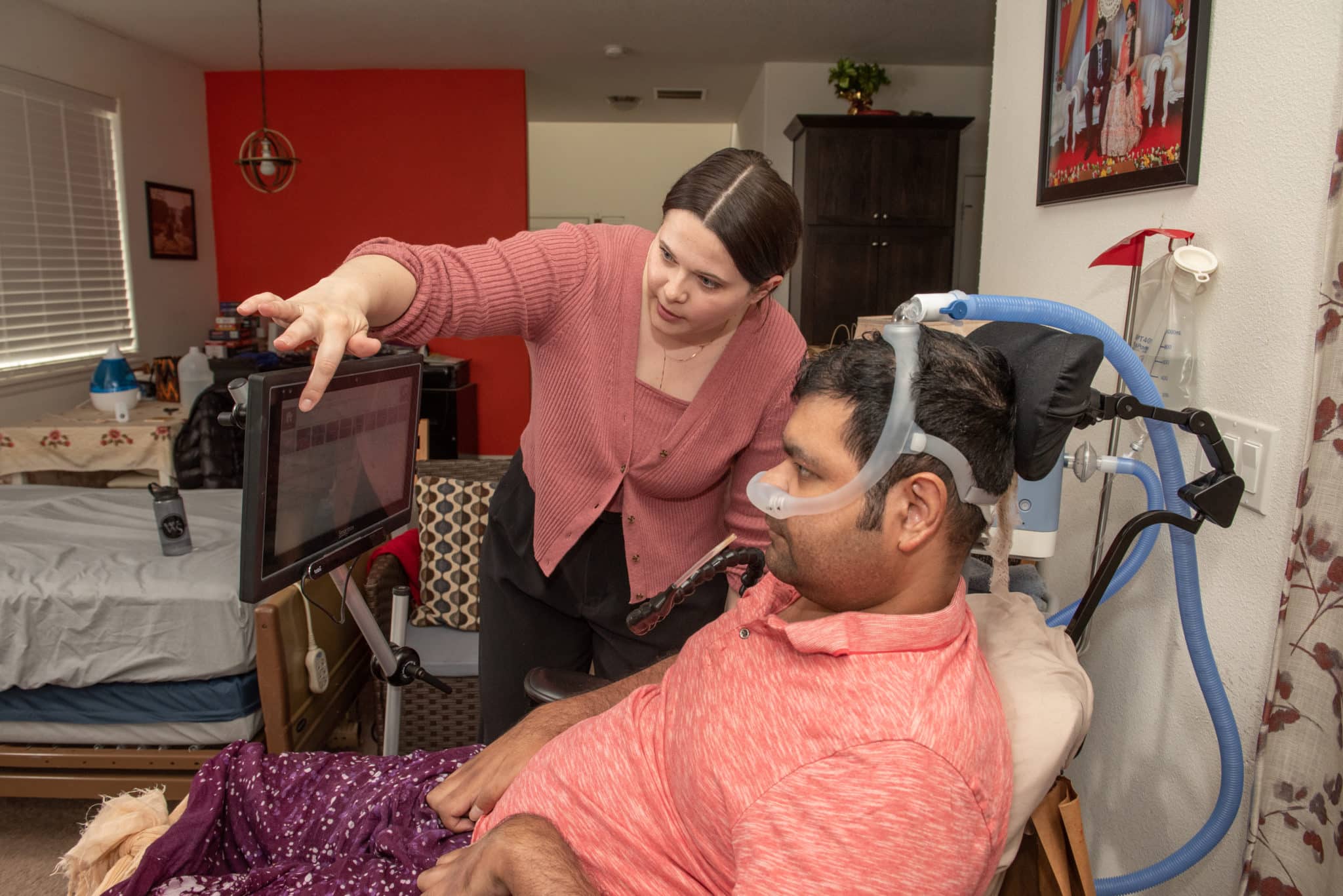 Staff member Ashley demonstrates assistive technology with person with ALS, Humed