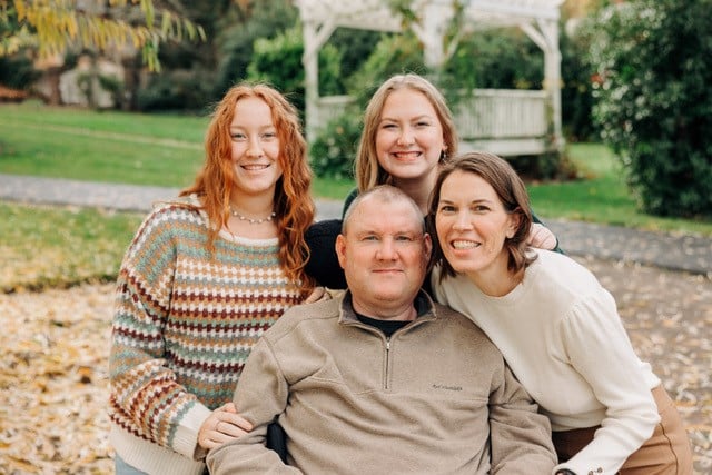 Cory Fox sits in his wheelchair in the middle, with his two daughters and wife Lacy around him